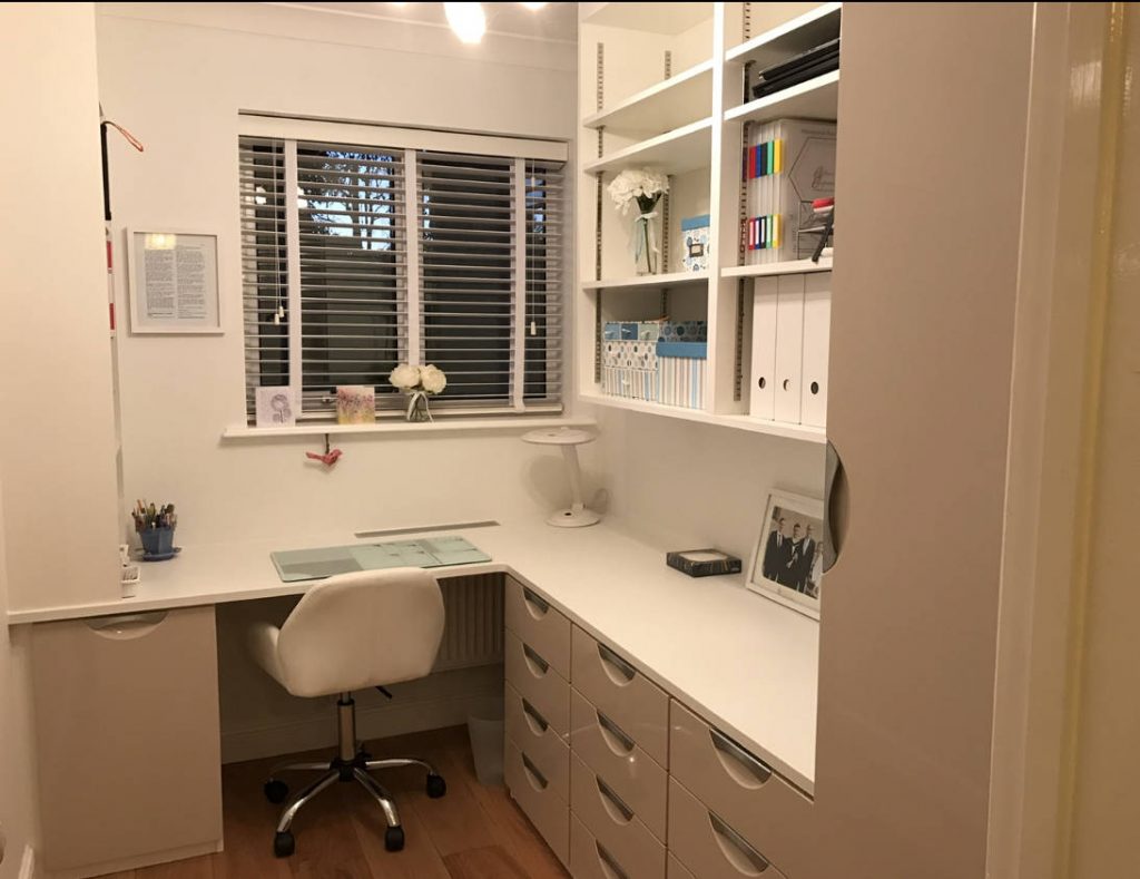 A fitted home office in white. There is a desk, chair, and drawers.